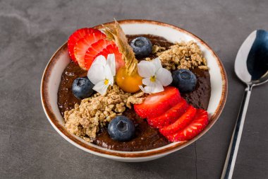 Granola, böğürtlen ve yenilebilir çiçeklerle kaplı tropik çikolata kasesi.