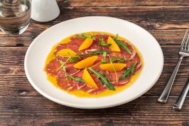 İnce dilimlenmiş et carpaccio portakal dilimleri ve roka yapraklarıyla.