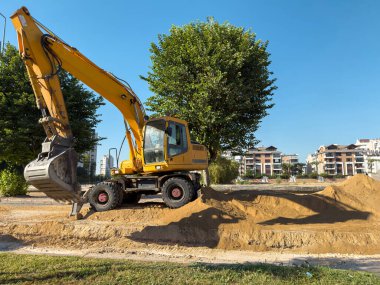 Sarı kazıcı mavi gökyüzünün altındaki kumlu inşaat sahasında çalışıyor