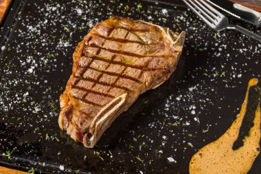 Lezzetli New York bifteği orta pişmiş ve siyah tabakta servis ediliyor.