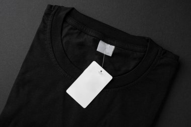 Folded black t-shirt with blank paper tag on dark background
