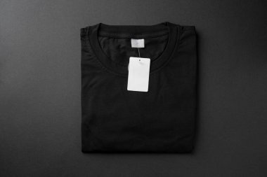 Folded black t-shirt with blank paper tag on dark background