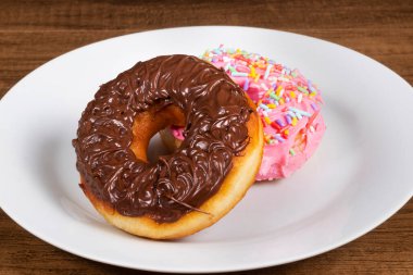 Çikolata kremalı tatlı çörekler ve pembe kremalı başka bir donut ve bir tabakta servis edilen renkli şekerlemeler. Yemek merkezli yakın çekim fotoğraf..