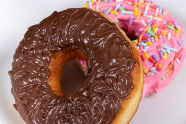 Çikolata kremalı tatlı çörekler ve pembe kremalı ve renkli bir tabakta servis edilen başka bir donut..