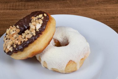 Kremalı tatlı çörekler ve pudralı süt kreması ve çikolata ve kestane şekerli ve fındıklı başka bir donut tabakta servis ediliyor..