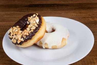 Kremalı ve sütlü tatlı çörekler ve beyaz tabakta servis edilen çikolata, kestane ve ceviz kaplı başka bir donut..