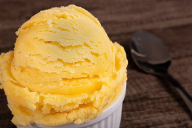 Vanilyalı dondurma bir kaşığın yanında beyaz bir kasede servis edilir. Sol arka planda sıralanmış yiyecekler bulanıklaştırıldı .