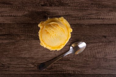 Sarı dondurma bir kaşığın yanında beyaz bir porselen tencerede servis edilir. Üst açı fotoğrafçılığını kapat.