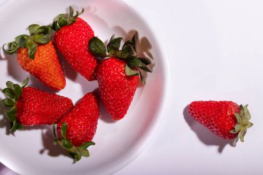 Beyaz arka planlı beyaz bir kasede servis edilen kırmızı çilekler.