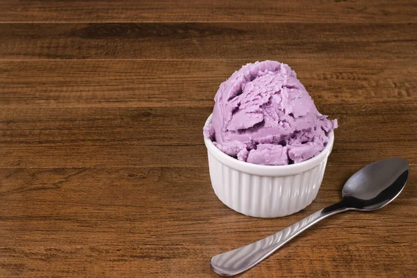 Grape-flavored purple ice cream with spoon on the side on a wooden table. Gastronomic photography with elements on the right with free space for text.