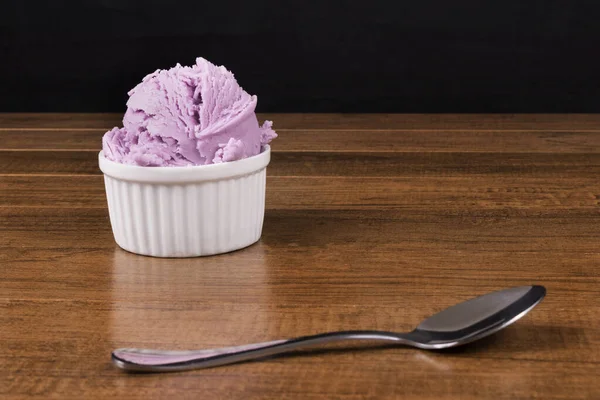 Grape-flavored purple ice cream on the wooden table. Spoon blurred in front of ice cream. Gourmet photo.