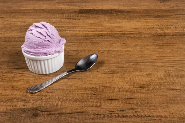 Grape-flavored purple ice cream served in the pot. A ball of ice cream accompanied by a spoon. Left-aligned elements leaving free space for text on the right.