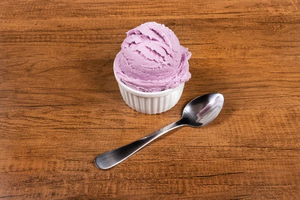 Grape-flavored purple ice cream served in the pot. A ball of ice cream accompanied by a spoon. Elements aligned to the center of the image.