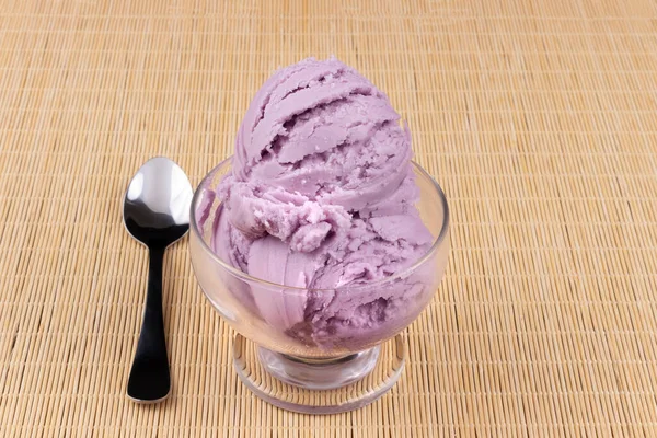 Glass bowl of purple grape flavored ice cream with three scoops of ice cream. Spoon left. Gastronomic close-up photography of ice cream