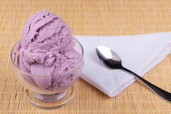 Tasty Grape-flavored purple ice cream served in a bowl with a spoon on the side on a white napkin. Gastronomic photography close-up desserts and frozen foods.