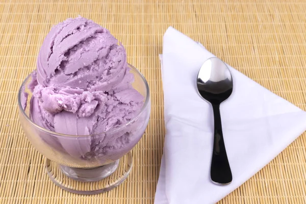 Grape-flavored purple ice cream served in a bowl with a spoon on the side on a white napkin.