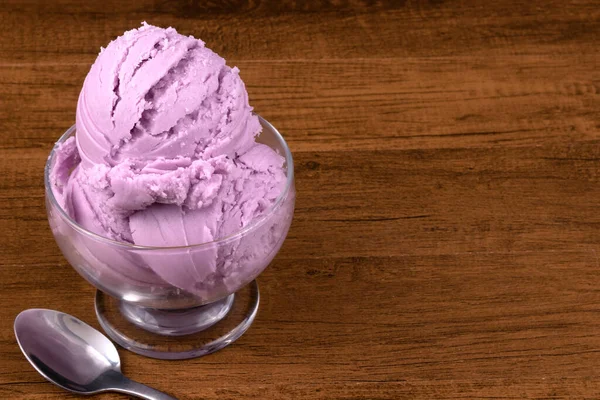Grape-flavored purple ice cream served in a glass bowl, beside a spoon. Empty space for texts on the right.