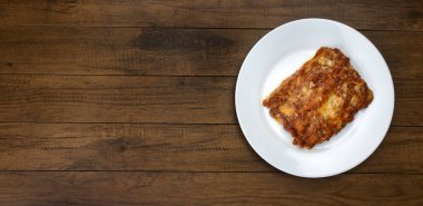 Bolonez soslu lazanya, jambon peyniri, domates sosu ve kıyma. Beyaz bir tabakta servis edilmiş. Panoramik üst görünüm fotoğrafı. Açık hava..