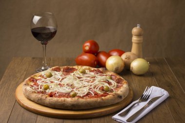 Lezzetli sucuklu sosisli pizza dilimleri soğan, mozzarella peyniri ve yeşil zeytin. Eşlik edecek lezzetli bir bardak kırmızı şarap. Fotoğrafı hazırlamak için kabuklu soğan ve domates..