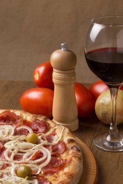 Soğan dilimleri, mozarella peyniri ve yeşil zeytinli epperoni pizza. Bir bardak şarap, soğan ve kırsal domates. Metinler için sol üst boşluğu olan Dikey Gurme Fotoğrafçılığı.