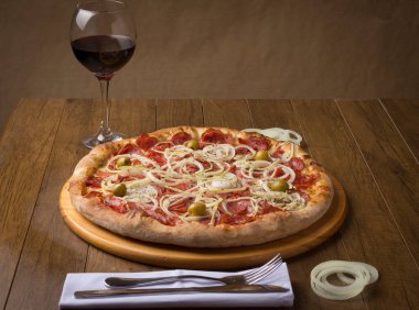 Biberli pizza, soğanlı ve yeşil zeytinli. Lezzetli yemeğe eşlik etmesi için bir bardak kırmızı şarap..