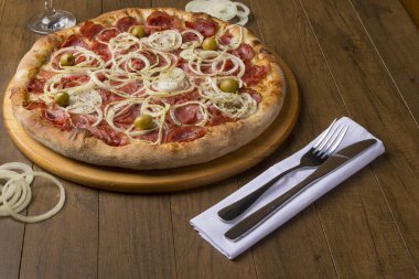 Pepperoni pizza, soğan dilimleri, mozzarella peyniri ve yeşil zeytin. Beyaz bir peçeteye çatal ve bıçak. Gurme fotoğrafçılık.