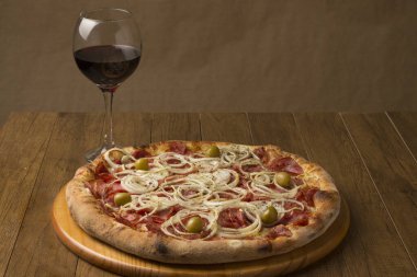 Biberli pizza, soğanlı ve yeşil zeytinli. Yiyeceğe eşlik etmesi için bir bardak kırmızı şarap. Brezilya tipik yemekleri. Pepperonie 'nin pizzasına benziyor..