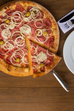 Pepperoni pizza, soğan dilimleri, mozzarella peyniri ve yeşil zeytin. Bir dilim pizzayı kaldırıyorum. Mesajlar için alt uzay. Dikey fotoğrafçılık.