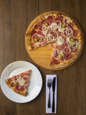 Pepperoni pizza, soğan dilimleri, mozzarella peyniri ve yeşil zeytin. Tabakta servis edilen bir dilim pizza. Dikey üst çekim.