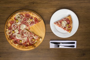 Pepperoni pizza, soğan dilimleri, mozzarella peyniri ve yeşil zeytin. Beyaz tabakta yenmeyi bekleyen lezzetli bir dilim pizza..