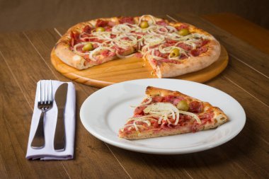 Soğan dilimleri, mozzarella peyniri ve yeşil zeytinlerle yapılan bir dilim pepperoni pizzası. Tabakta pizza var. Gastronomik yemek fotoğrafçılığı.