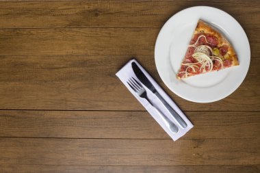 Biberli pizza dilimi soğan dilimleri, mozzarella peyniri ve yeşil zeytinlerle yapılır. Beyaz bir peçeteye çatal ve bıçak. Metin için sol boşluk.