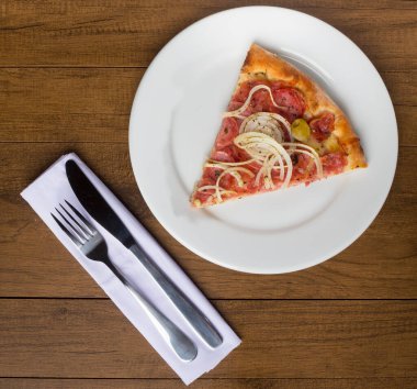 Biberli pizza dilimi soğan dilimleri, mozzarella peyniri ve yeşil zeytinlerle yapılır. Beyaz bir peçeteye çatal ve bıçak. Gastronomik fotoğrafçılık.