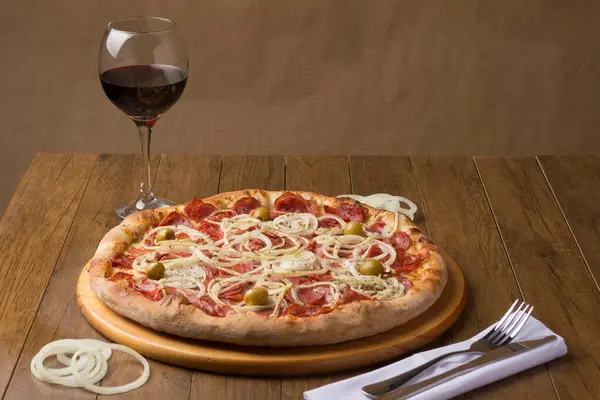Pepperoni sausage pizza with slices of onions and green olives. Glass of Red Wine to accompany the meal. Typical Brazilian food from Italy. Similar to Pepperonie\'s pizza.