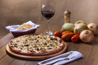 Tahtada etli pizza. Mozzarella, picanha eti, soğan, peynir, domates sosu. Biftek, et, biber öğütücü, bir bardak kırmızı şarap, crostini, çatal ve bıçak. Yatay yüksek açı.