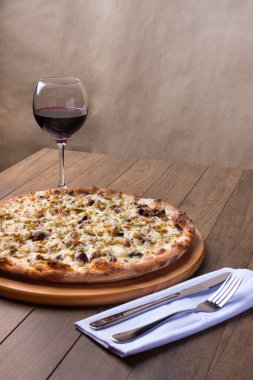 Tahtada etli pizza. Mozzarella, picanha eti, soğan, peynir, domates sosu. Biftek, et, bir bardak kırmızı şarap, çatal ve bıçak. Gurme dikey fotoğraf.