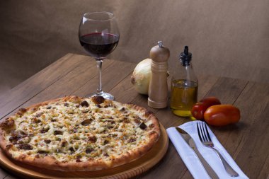 Tahtada etli pizza. Mozzarella, picanha eti, soğan, peynir, domates sosu. Biftek, et, biber öğütücü, bir bardak kırmızı şarap, crostini, çatal ve bıçak. Yüksek açılı fotoğraf.