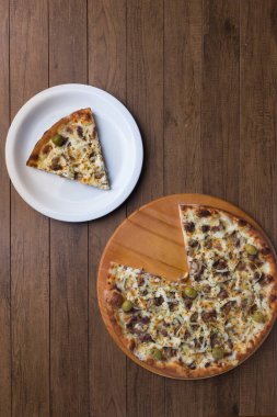 Tahtada etli pizza. Mozzarella, picanha eti, soğan, peynir, domates sosu ve zeytinle yapıldı. Biftek, et. Beyaz bir tabakta servis edilen pizza ve dilimlenmiş pizza. Üst resim.