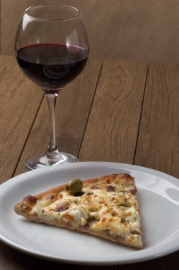 Tabakta servis edilen lezzetli bir dilim. Tahtada etli pizza. Mozzarella, picanha eti, soğan, peynir, sos ve zeytinle yapıldı. Biftek. Çatal ve Bıçak Kafa. Bir kadeh kırmızı şarap. Dikey.