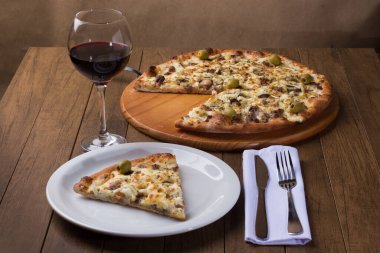 Tabakta servis edilen lezzetli bir dilim. Tahtada etli pizza. Mozzarella, picanha eti, soğan, peynir, sos ve zeytinle yapıldı. Biftek. Çatal ve Bıçak Kafa. Bir kadeh kırmızı şarap. Yatay.