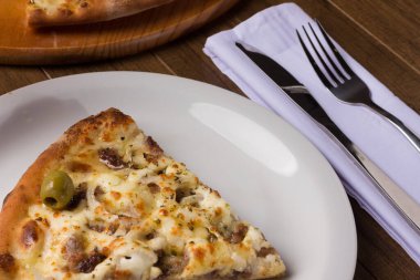 Tabakta servis edilen lezzetli bir dilim. Tahtada etli pizza. Mozzarella, picanha eti, soğan, peynir, sos ve zeytinle yapıldı. Biftek. Çatal ve Bıçak üstte. Makro.