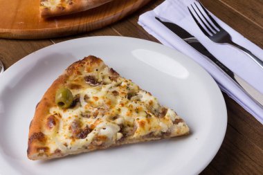 Tabakta servis edilen lezzetli bir dilim. Tahtada etli pizza. Mozzarella, picanha eti, soğan, peynir, sos ve zeytinle yapıldı. Biftek. Çatal ve Bıçak üstte. Ayrıntıları dilimle.