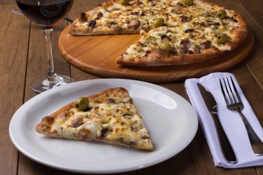 Tabakta servis edilen lezzetli bir dilim. Tahtada etli pizza. Mozzarella, picanha eti, soğan, peynir, sos ve zeytinle yapıldı. Biftek. Çatal ve Bıçak Üstü örtülü, şarap kadehi. Gurme.