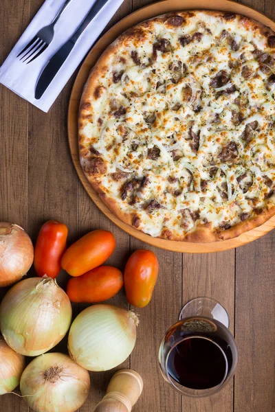 Meat pizza on wooden board. Made with Mozzarella, picanha meat, onion, cheese, tomato sauce. Filet Steak, meat, pepper grinder, glass of red wine, crostini, fork and knife. Vertical photo from the top