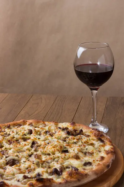 Delicious meat pizza on wooden board. Made with Mozzarella, picanha meat, onion, cheese, tomato sauce. Filet Steak, meat. Glass of red wine to accompany. Vertical photo.