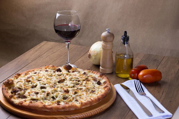 Delicious meat pizza on wooden board. Made with Mozzarella, picanha meat, onion, cheese, tomato sauce. Filet Steak, meat, pepper grinder, glass of red wine, fork and knife.