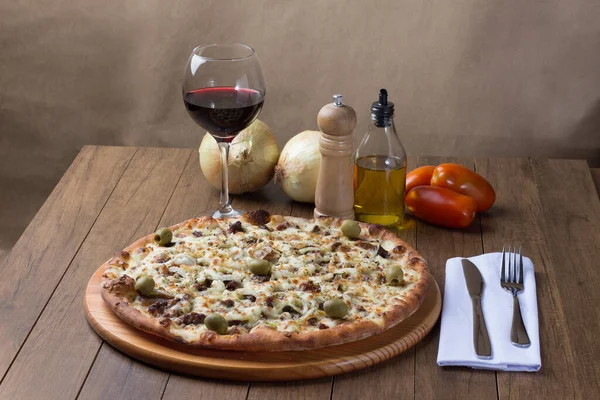 Meat pizza on wooden board. Made with Mozzarella, picanha meat, onion, cheese, tomato sauce and olives. Filet Steak, meat, pepper grinder, glass of red wine, crostini, fork and knife.