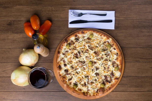 Meat pizza on wooden board. Made with Mozzarella, picanha meat, onion, cheese, tomato sauce and olives. Filet Steak, meat, pepper grinder, glass of red wine, fork and knife. Photo from the top
