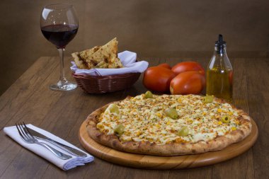 Akılda kalıcı tavuk aromalı pizza. Mozarella, tavuk, krem peynir, yeşil zeytin, mısır ve kırmızı domates sosuyla yapılmış. Kırmızı şarap, porsiyon crostini, zeytinyağı ile servis edilir. Çatal ve bıçak beyaz peçeteye. Yatay fotoğrafçılık.