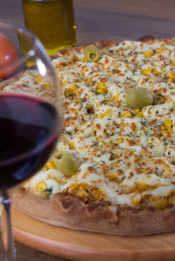 Akılda kalıcı tavuk aromalı pizza. Mozarella, tavuk, krem peynir, yeşil zeytin, mısır ve kırmızı domates sosuyla yapılmış. Kırmızı şarap ve zeytinyağıyla servis edilir. Bulanık şarap kadehiyle dikey fotoğraf.